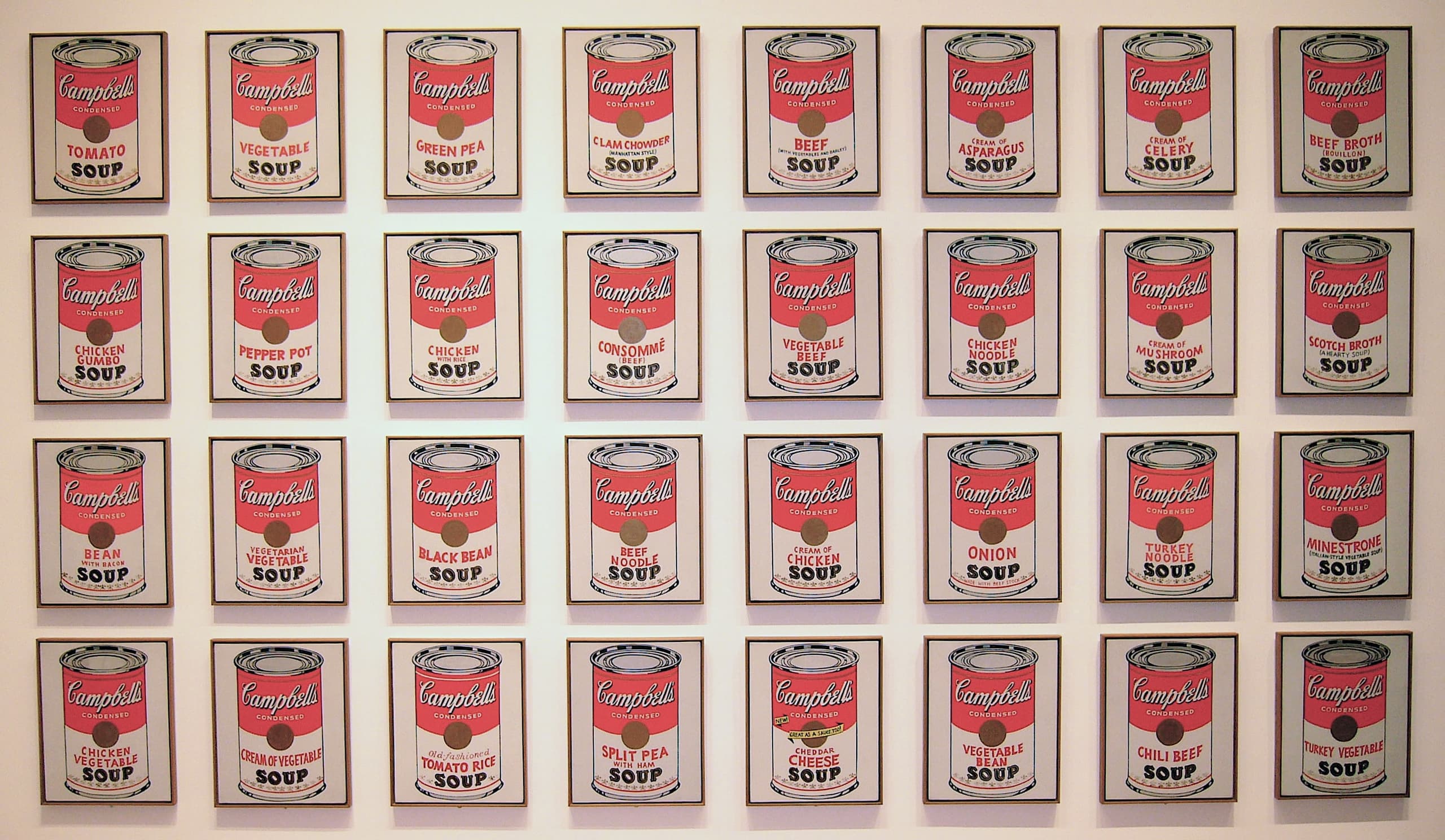 A regular grid of painted red-and-white soup cans on canvas, each label bearing a different variety name, hung together as one wide rectangular installation.