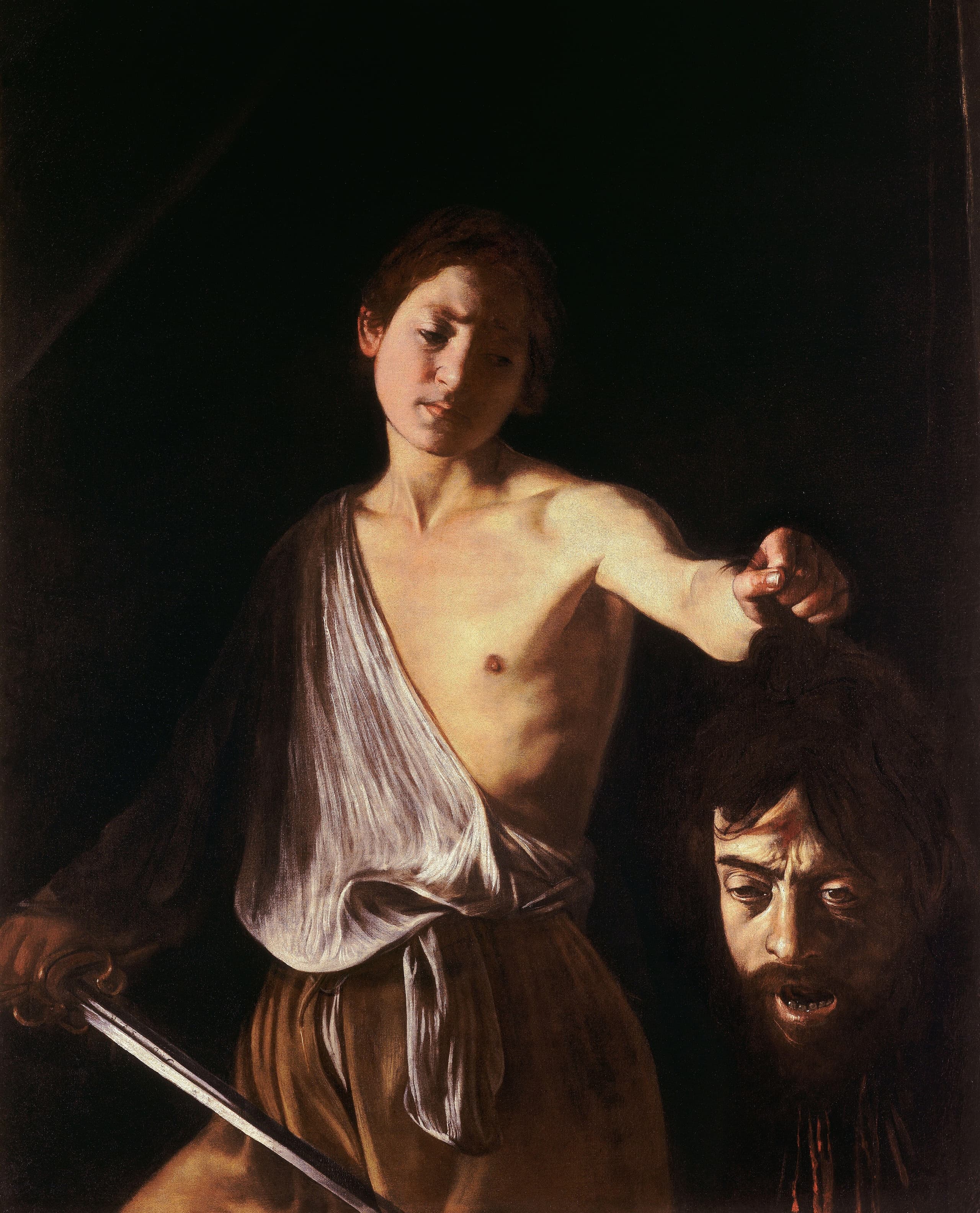 A bare-shouldered youth in deep shadow holds a sword in one hand and, by the hair, a severed bearded head in the other. Light strikes his chest and the slack face of the head; blood trails from the neck.