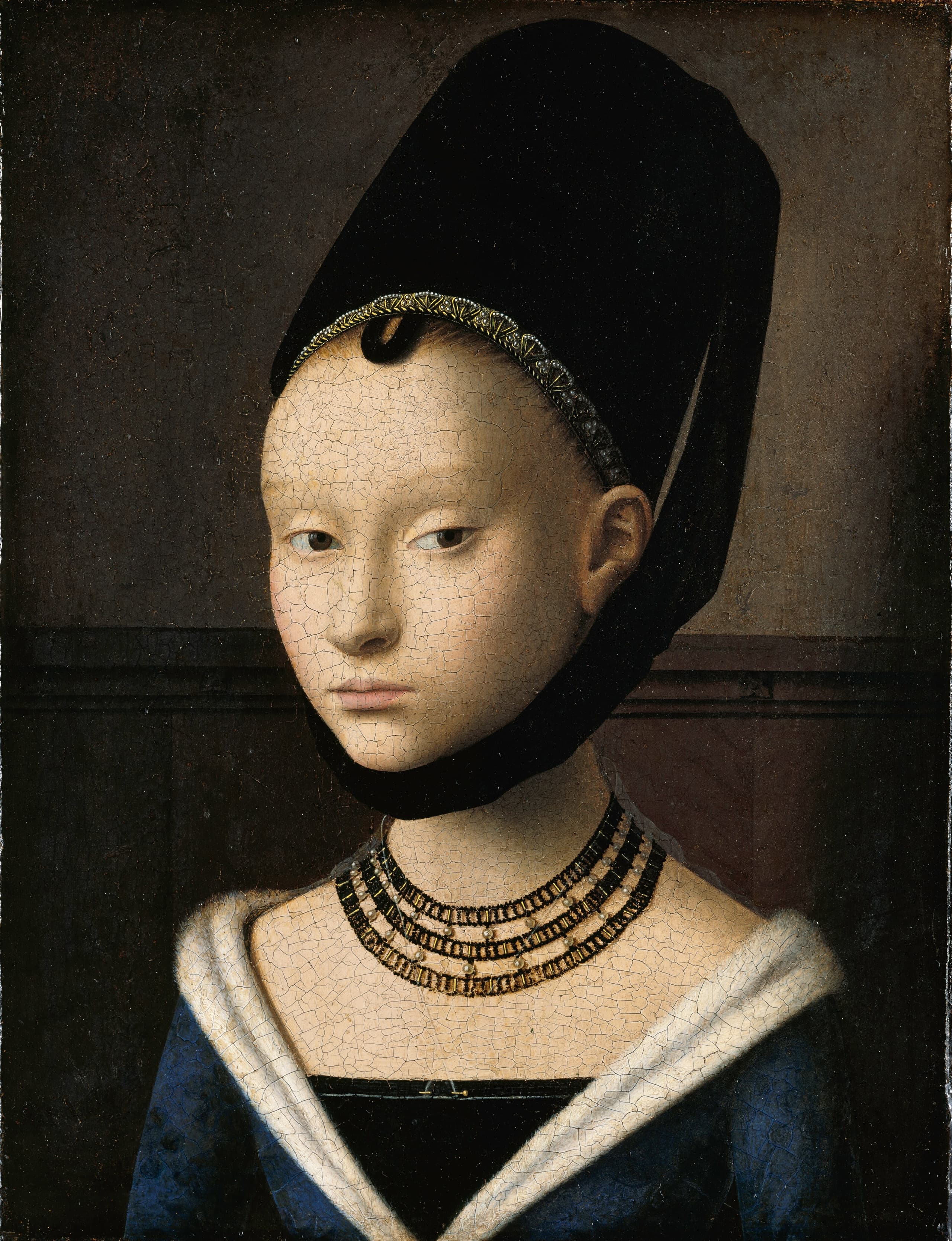 A young woman faces the viewer from a shallow, dim interior, pale face framed by a dark headdress, her expression steady and reserved against the quiet space around her.
