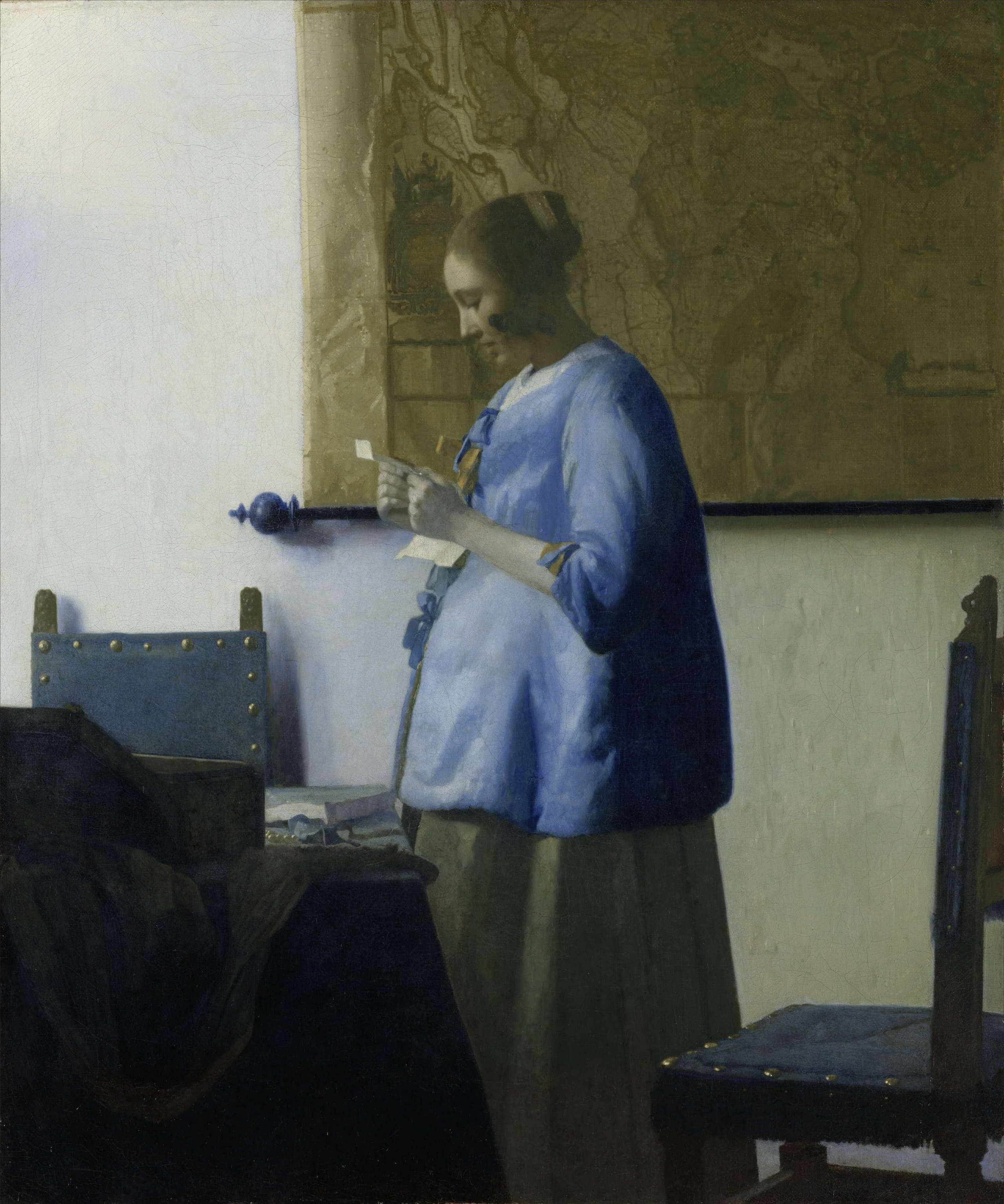 A woman in a blue garment stands in a quiet interior, head bent over a pale letter held in both hands, the small canvas tightly framed around her figure.