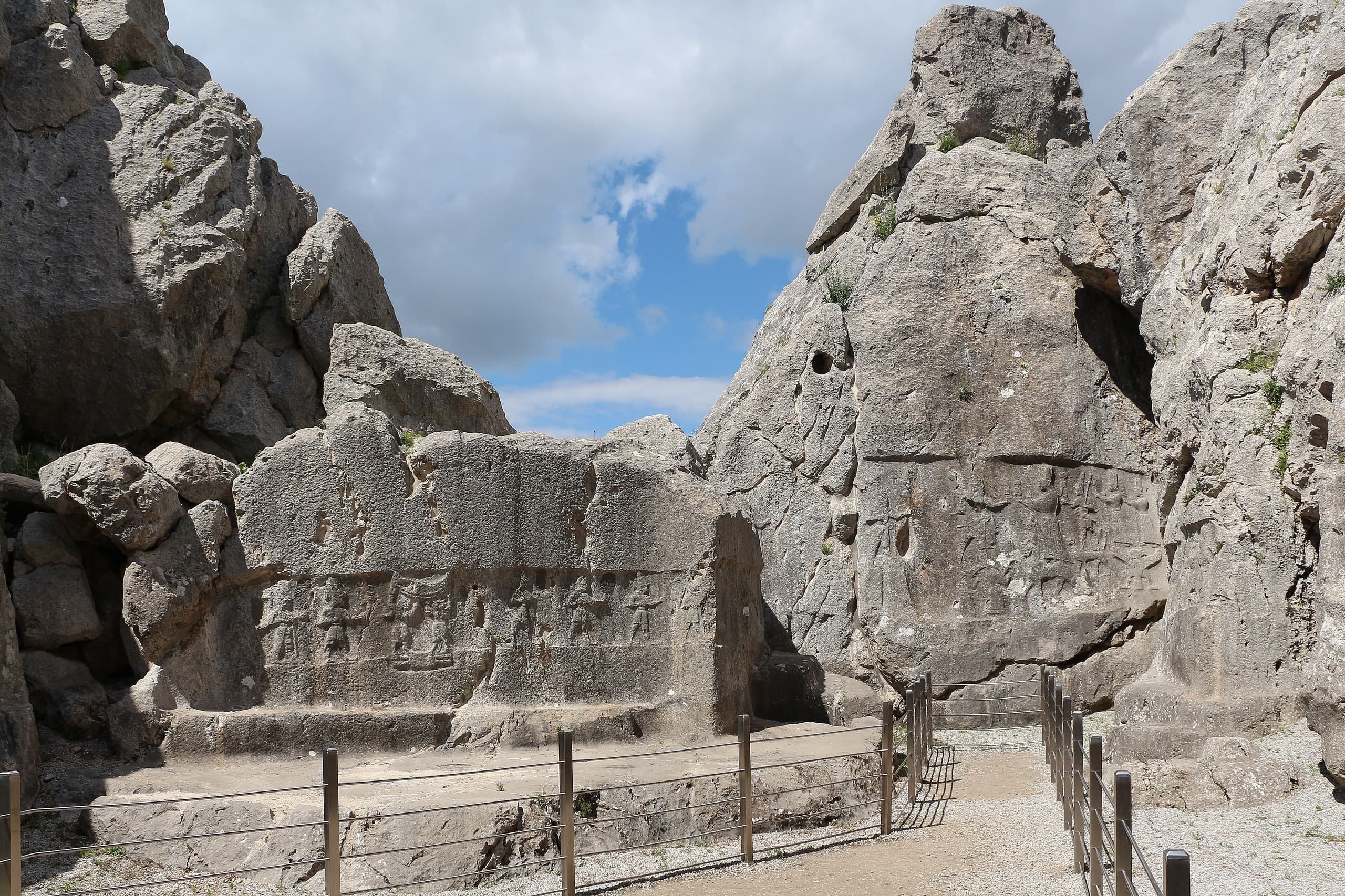 A natural rock face bearing carved figures arranged in horizontal zones, with a principal figure emphasised near the centre and smaller relief detail lower on the stone.