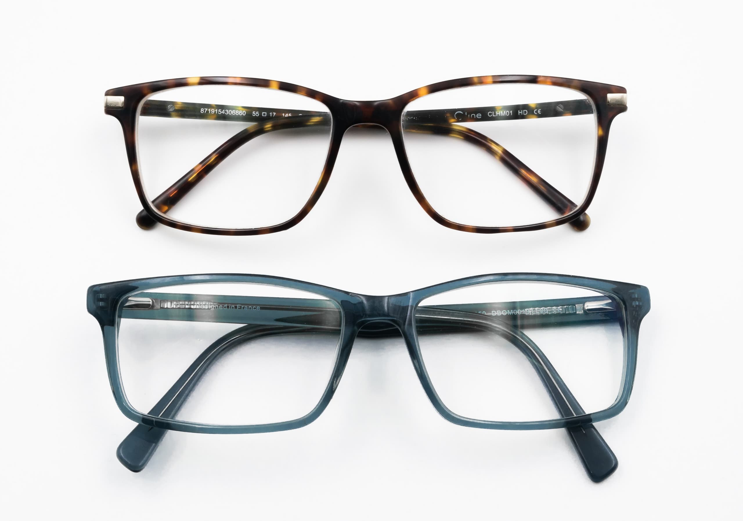 A pair of modern eyeglasses with clear lenses in a thin metal frame, resting on a flat surface, with temple arms extended.