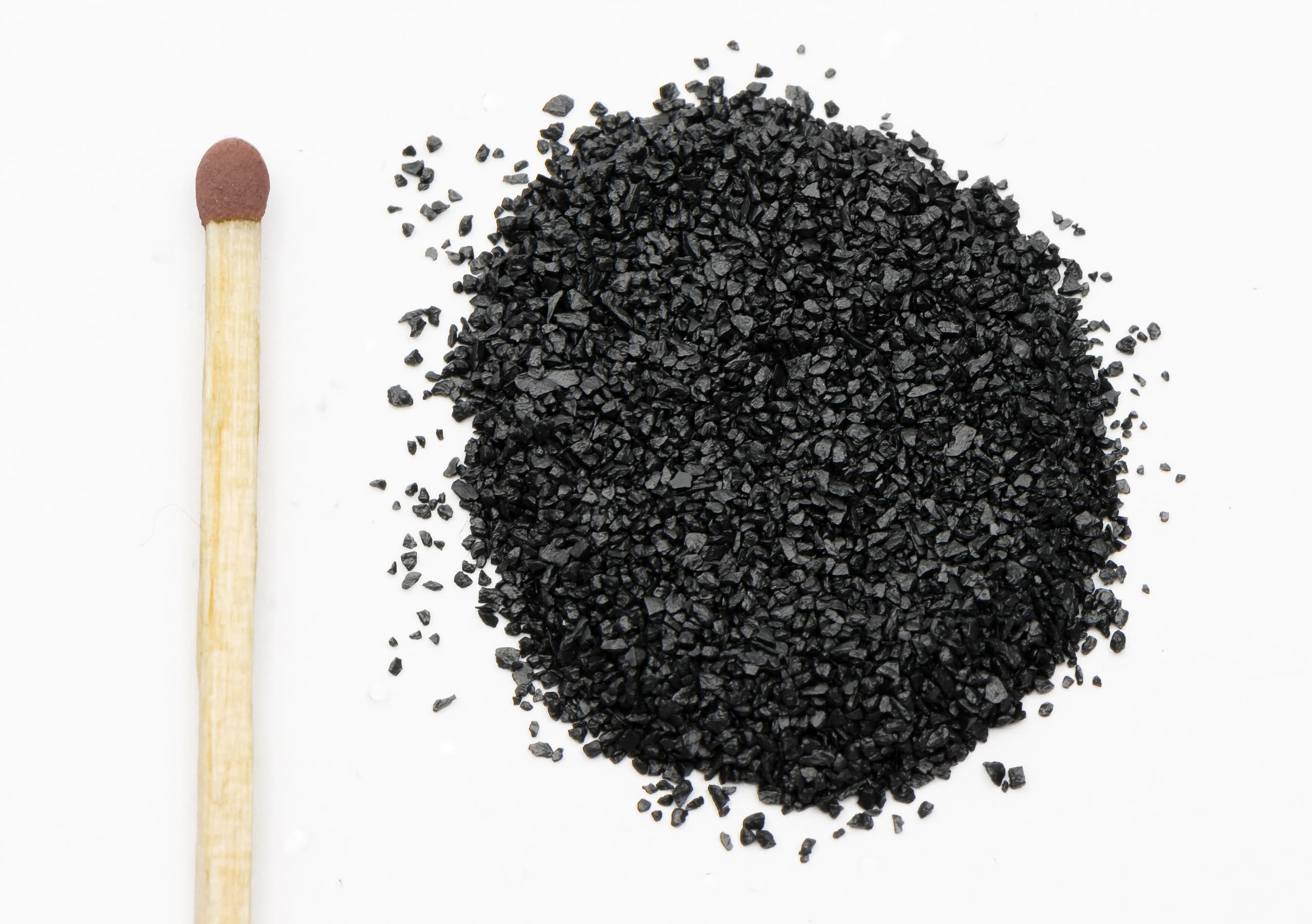 Three small mounds of powder on a white surface: pale yellow sulfur, black charcoal, and white crystalline potassium nitrate, the three components of gunpowder.