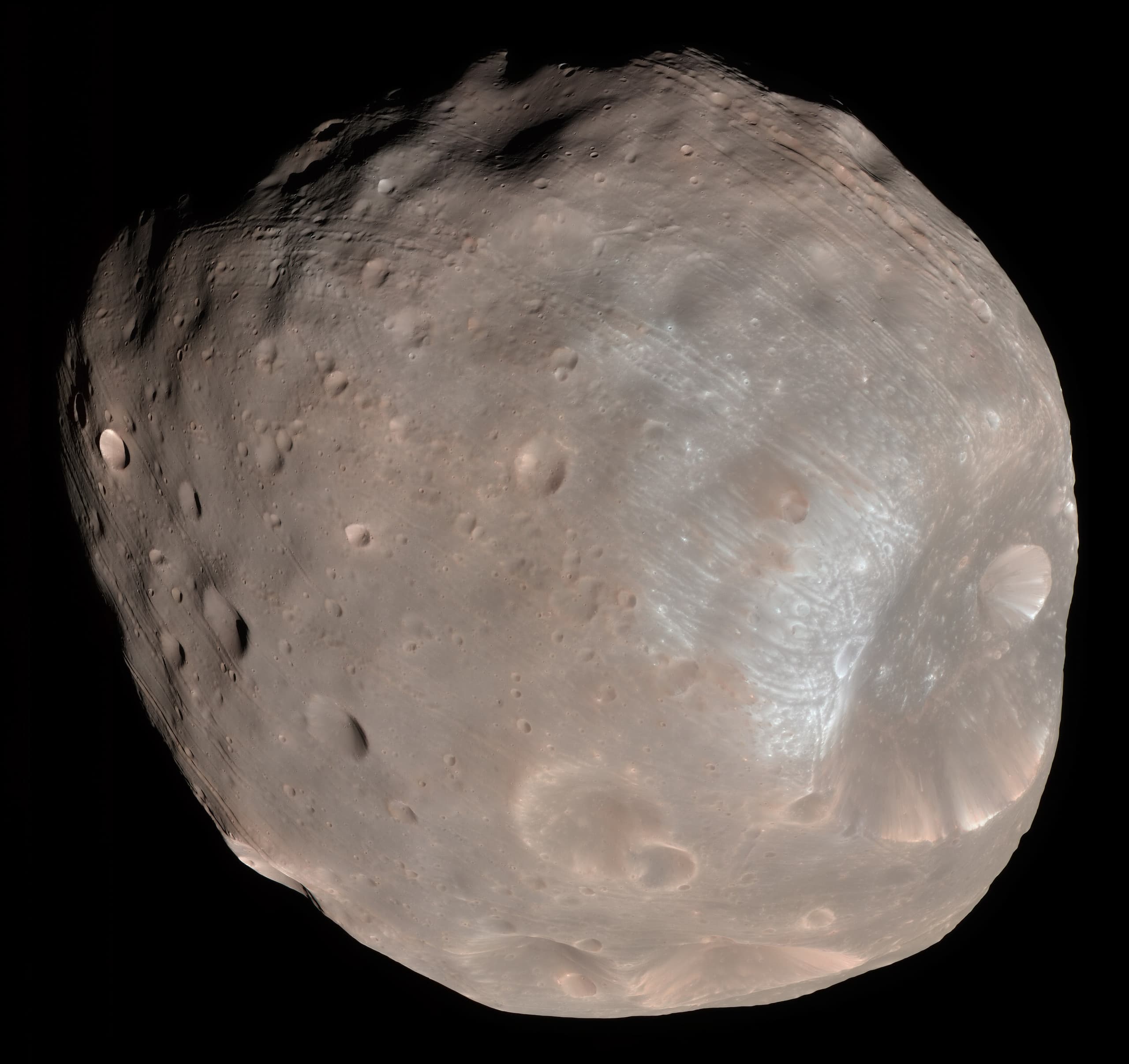 A small, irregularly shaped grey moon covered in craters, with one very large impact crater dominating one side, photographed against the black of space.
