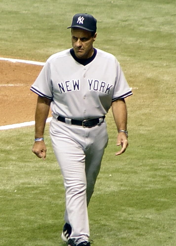 Head-and-shoulders portrait of a man in a white baseball uniform with dark pinstripes, a dark cap with a white interlocking logo on it, looking directly at the camera with a neutral expression.