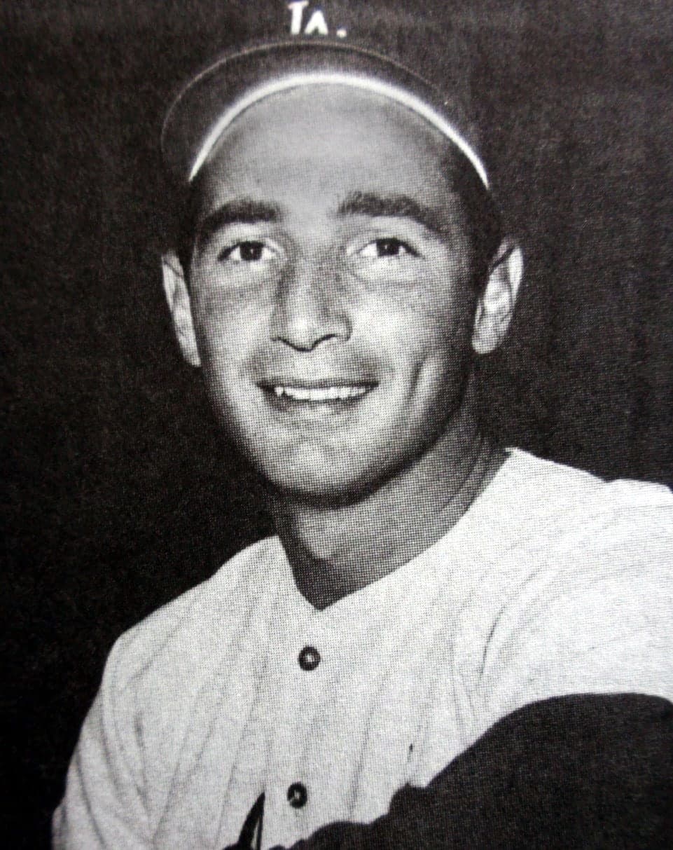 A left-handed pitcher in mid-delivery, his left leg raised high, his body coiled, wearing a white uniform with 'Dodgers' across the chest in script, a baseball cap with the letter D, and the number 32 visible on his back.