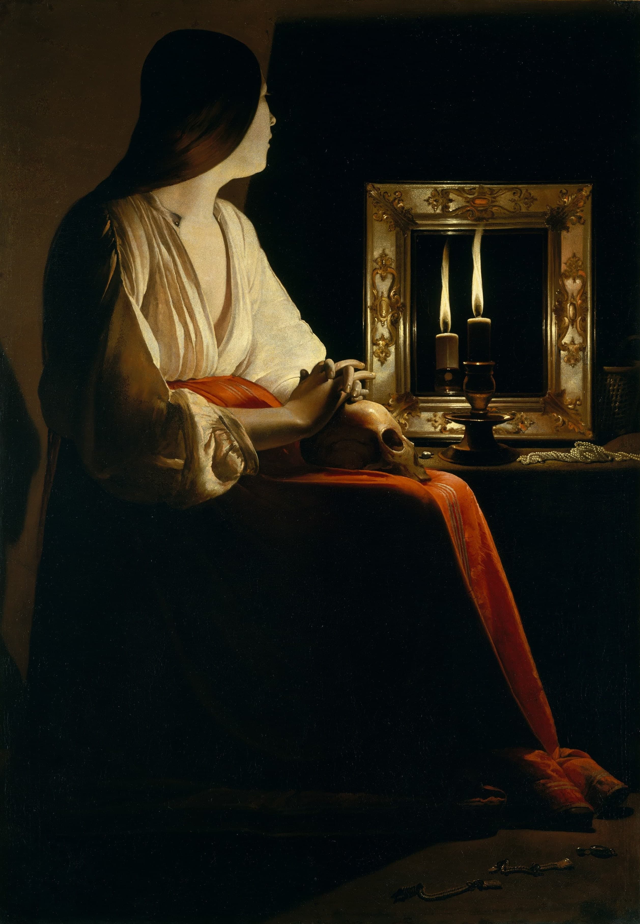 A seated woman in darkness, her face and breast lit by a candle; a mirror returns a second flame, and she holds a skull beside discarded jewellery.