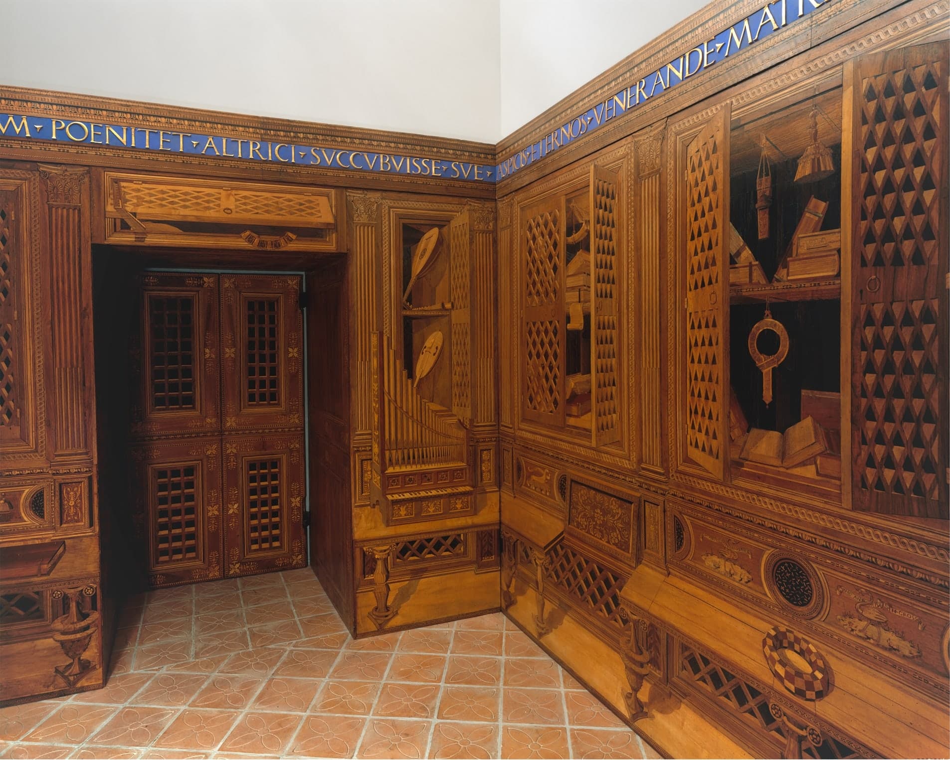 A small wood-panelled room with intarsia panels covering the walls, depicting books, instruments, and architectural elements in perspective, all made from different-coloured wood veneers fitted together.