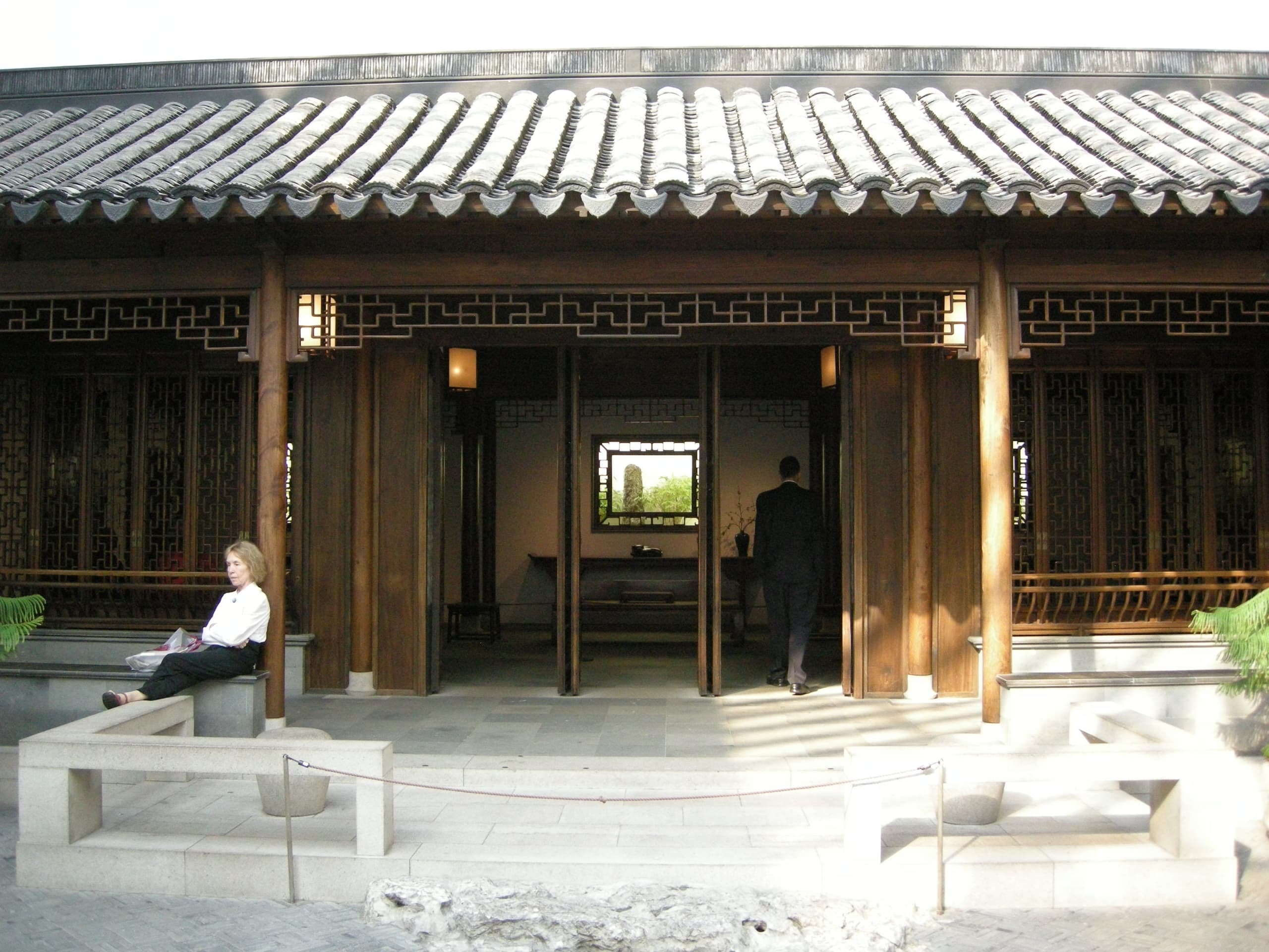 An enclosed Chinese-style courtyard garden with traditional timber architecture, stone paving and plantings, held within the walls of a museum gallery.